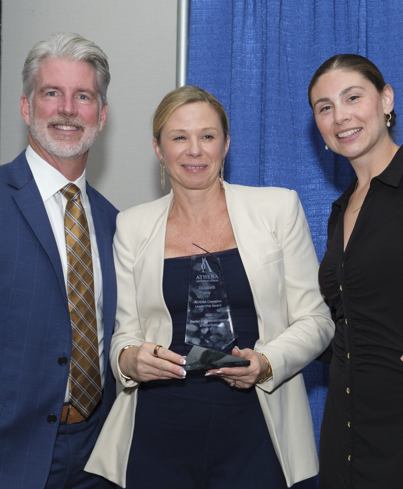 Three people smiling. The person in the center holds a glass award.
