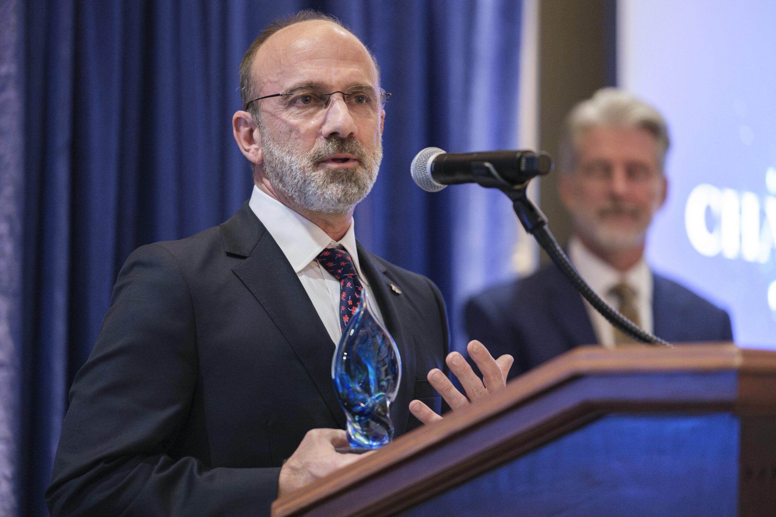 Person speaking at podium, holding glass award.